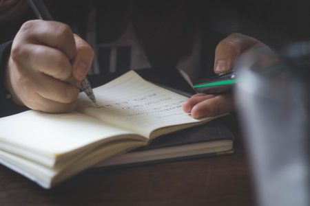 Close up of man on his smartphone while writing in a notebook.