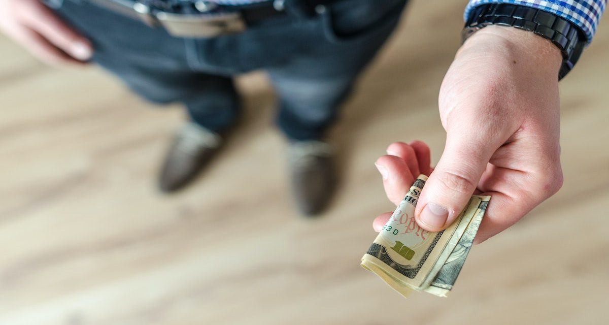 An image of a man with his hand extended, with a few folded up bills in it