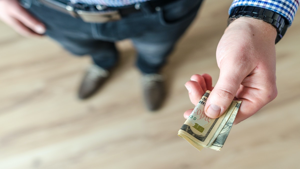 An image of a man with his hand extended, with a few folded up bills in it