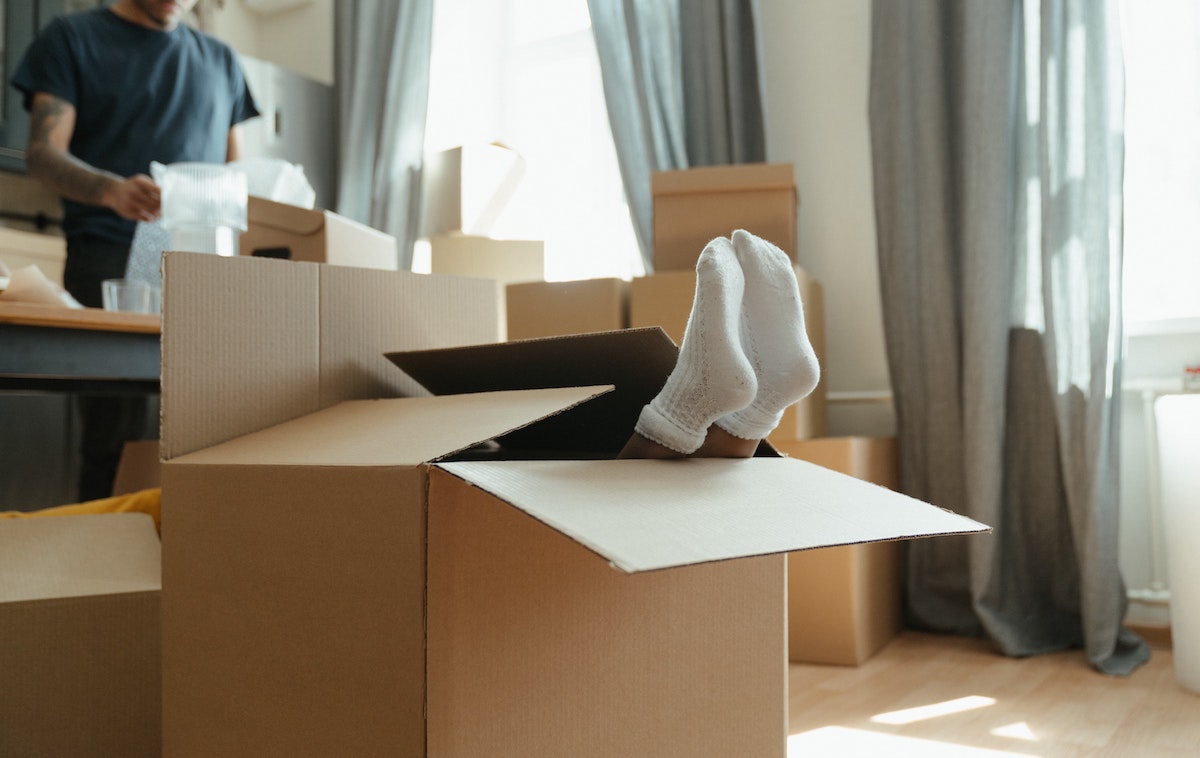 Millennial real estate is taking off. A picture of a man getting packing materials ready for a move, with a box in front with feet sticking out of it.