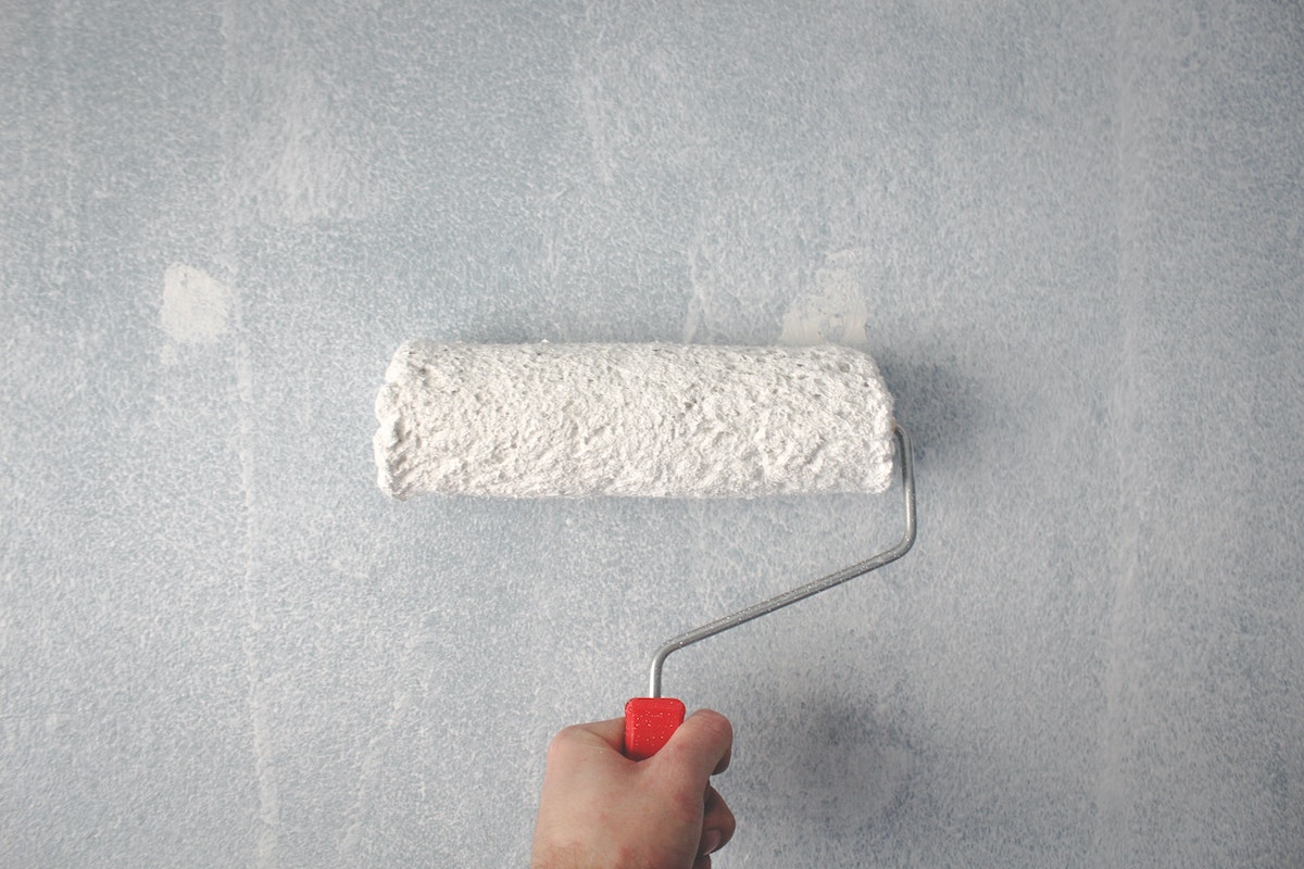 ARV in real estate can be boosted by painting the house. This is a picture of a person holding a paint roller against a wall.