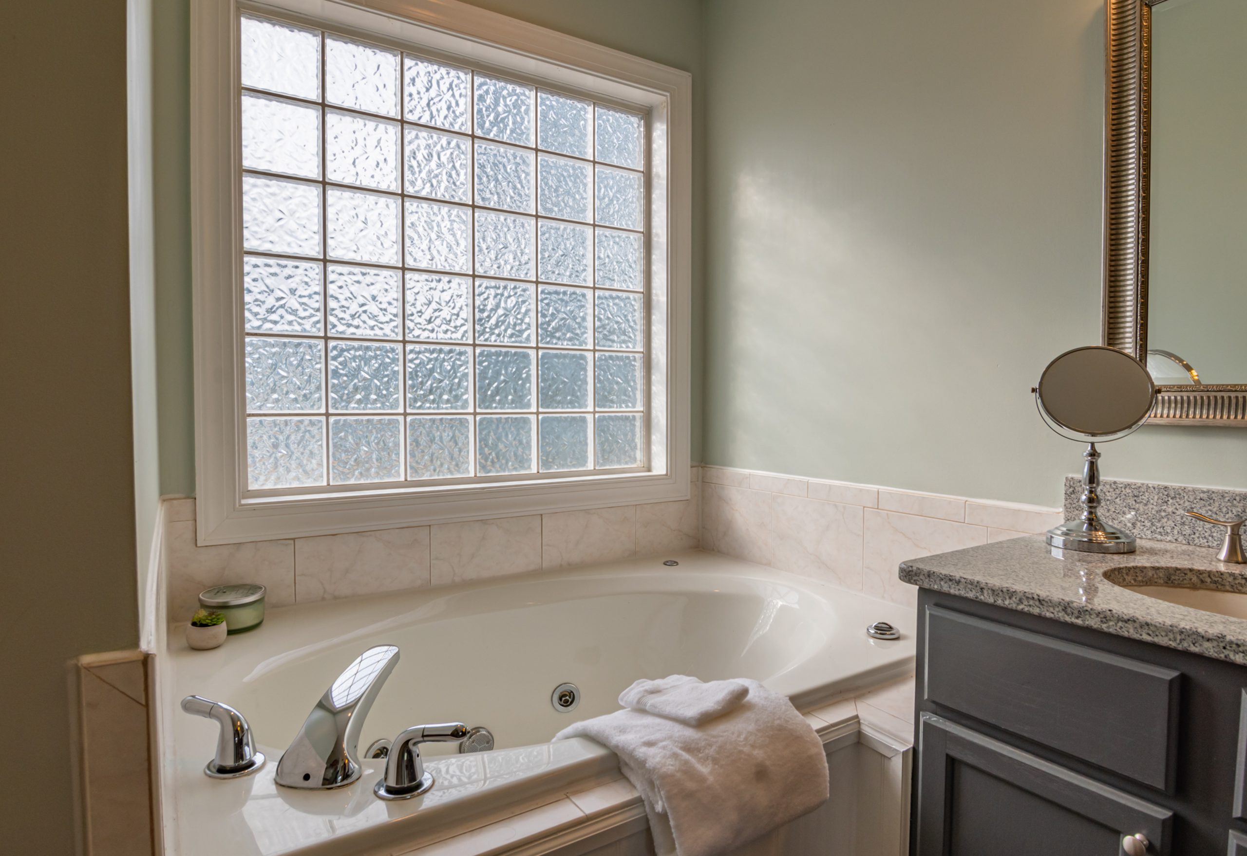 ARV in real estate can take a hit if you just have a tub in your bathroom. This picture shows a tub with towels draped over the sides. There's a window above the tub. To the right side you can see a sing with a small mirror on top.