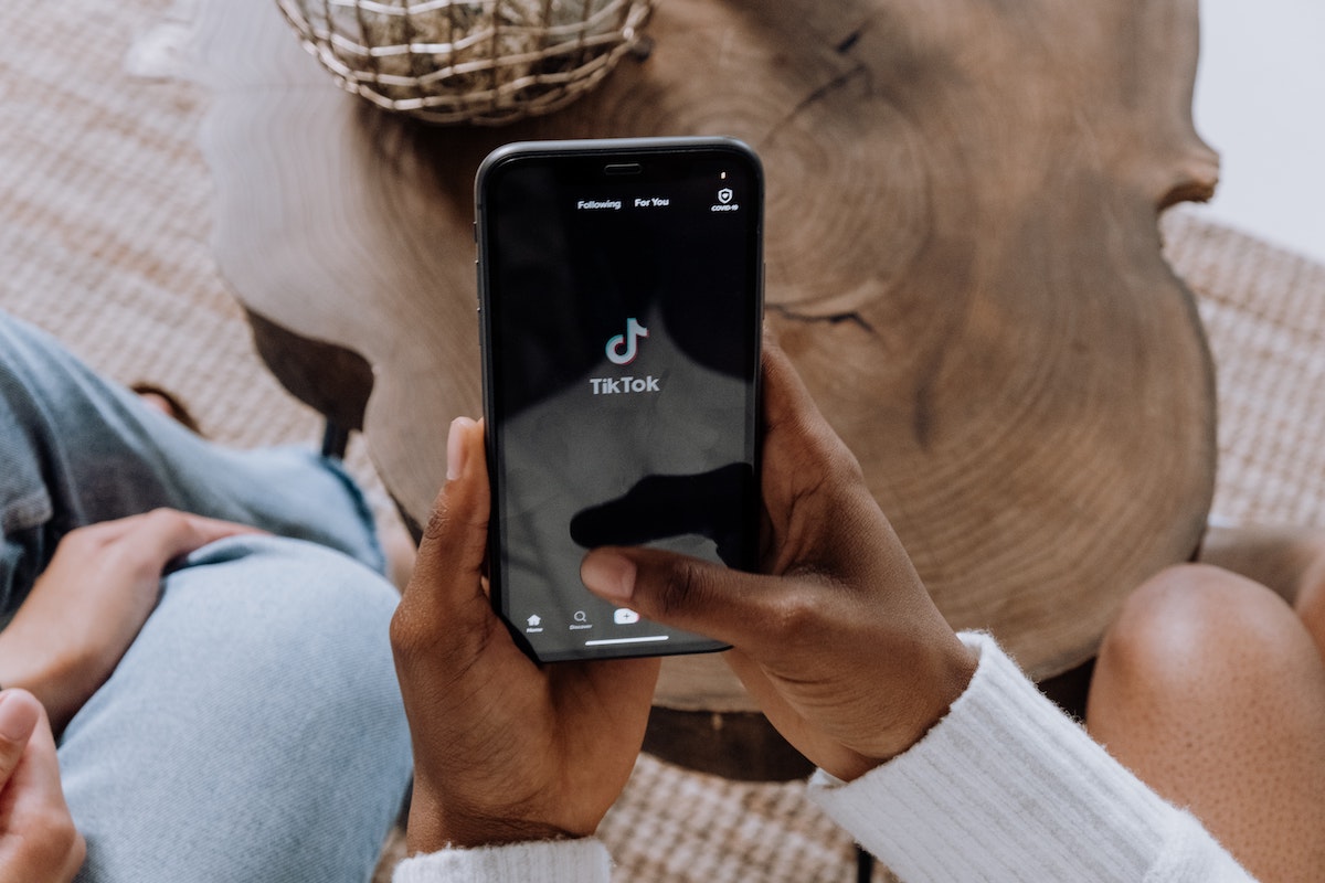 An image of someone holding a phone with the TikTok logo on the phone screen. "Real Estate Tiktok" has become a popular way for real estate agents to attract new home buyers.